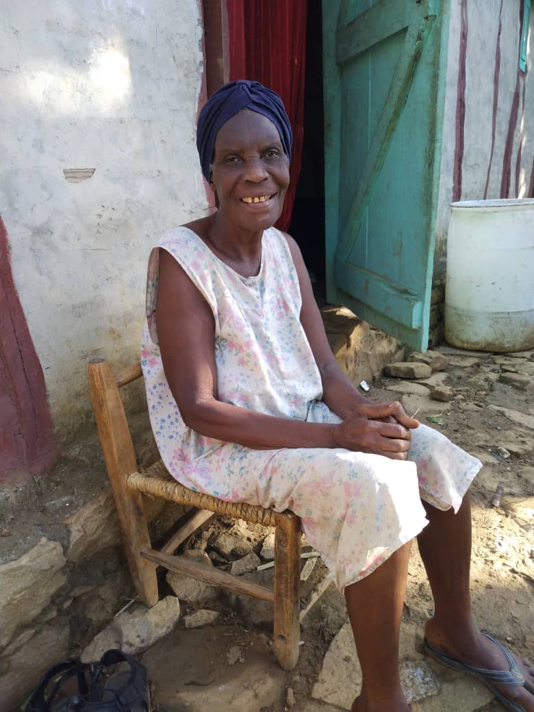 Aprelie, a blind widow from rural Haiti, seated outside her home.